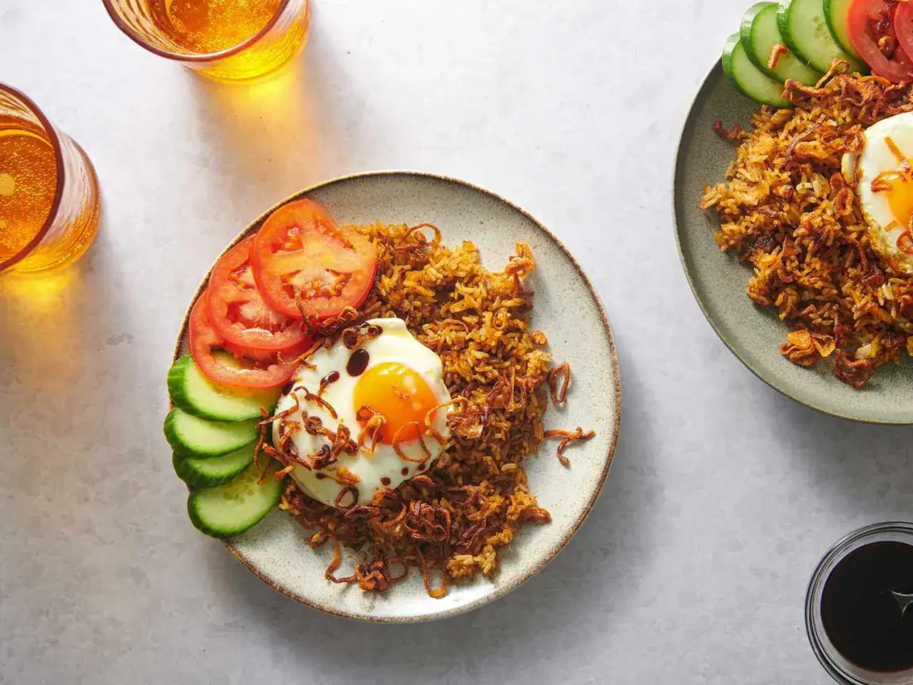 Zwei Teller mit Nasi Goreng, garniert mit Spiegelei, Tomaten und Gurken. Ein köstliches indonesisches Gericht!