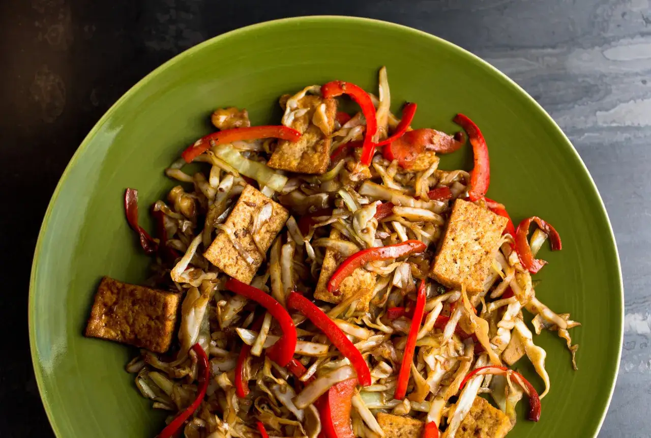 Ein Gericht mit spitzkohl asiatisch vegetarisch, gebratenem Tofu und roten Paprikastreifen auf einem grünen Teller.