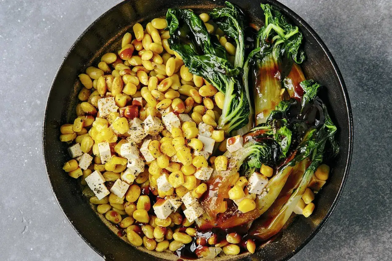 Sojabohnen zubereiten: Gelbe Sojabohnen, Mais und gew&uuml;rfelter Tofu in einer Pfanne mit glasiertem Pak Choi und dunkler Sauce.