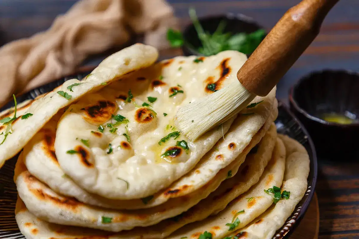 Frisch gebackenes Naan Brot, bestrichen mit Butter und garniert mit Petersilie. So wird dieses k&ouml;stliche Fladenbrot zubereitet.