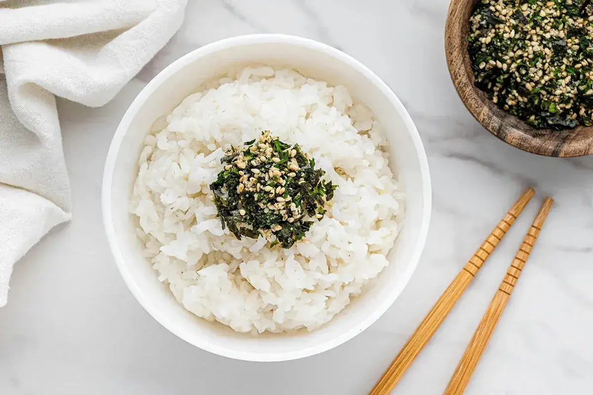 Schüssel mit Reis und einer Portion selbstgemachtem Furikake, garniert mit Sesam und Algen. Stäbchen liegen daneben.