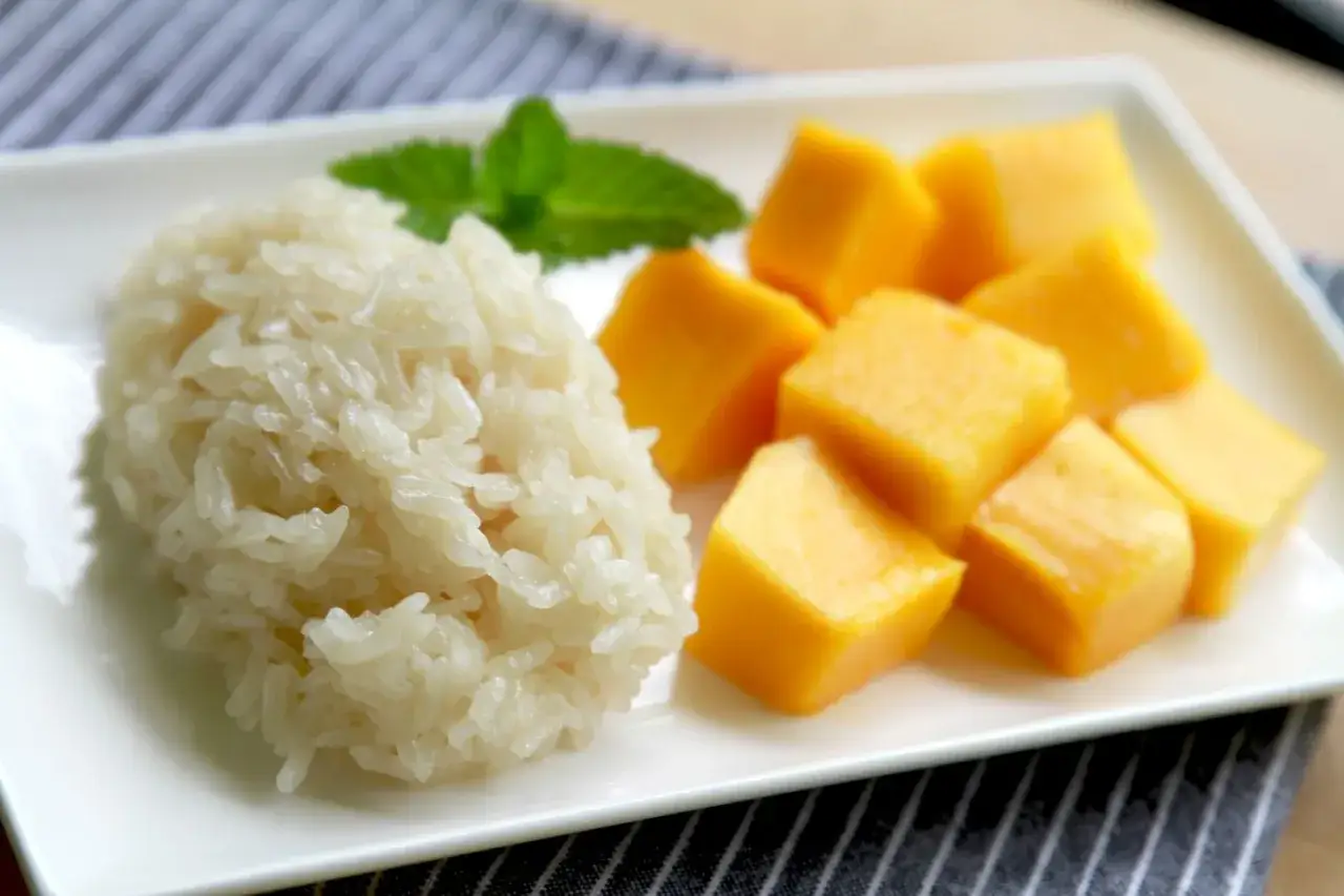 Ein Teller mit s&uuml;&szlig;em Mango-Klebreis, garniert mit Minze. Der Klebreis ist perfekt gekocht und welcher Reis klebt, ist hier deutlich zu sehen.