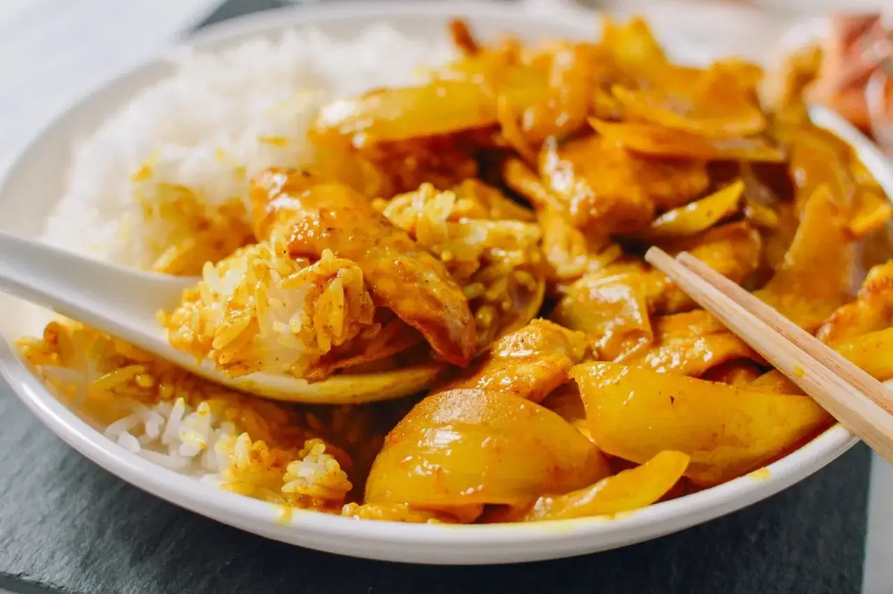 Ein L&ouml;ffel voller asiatischer Reis mit H&uuml;hnchen-Curry. Chopsticks liegen bereit f&uuml;r die n&auml;chste Portion.