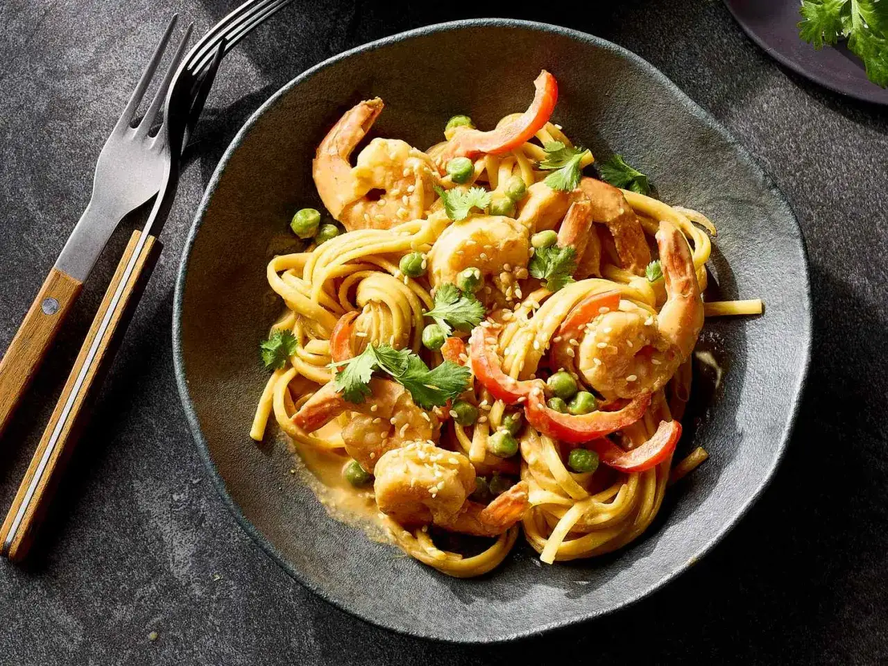 Mi Quang Nudeln mit Garnelen, Erbsen und Paprika in cremiger Sauce, garniert mit Koriander und Sesam.