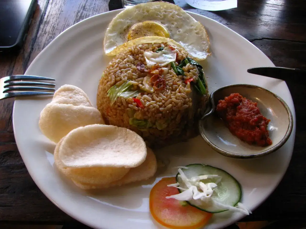Ein Teller mit Nasi Goreng, garniert mit einem Spiegelei, Garnelenchips und scharfer Sambal. Ein authentisches nasi goreng rezept original.
