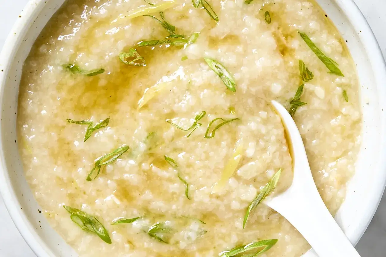 Cremiger Reis Congee mit Ingwer und Fr&uuml;hlingszwiebeln, serviert in einer Sch&uuml;ssel mit einem L&ouml;ffel.