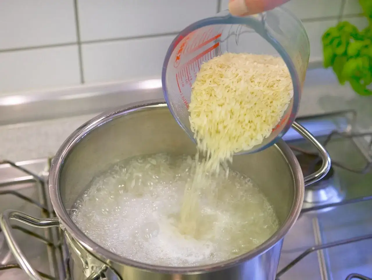 Parboiled Reis wird aus einem Messbecher in kochendes Wasser gesch&uuml;ttet.