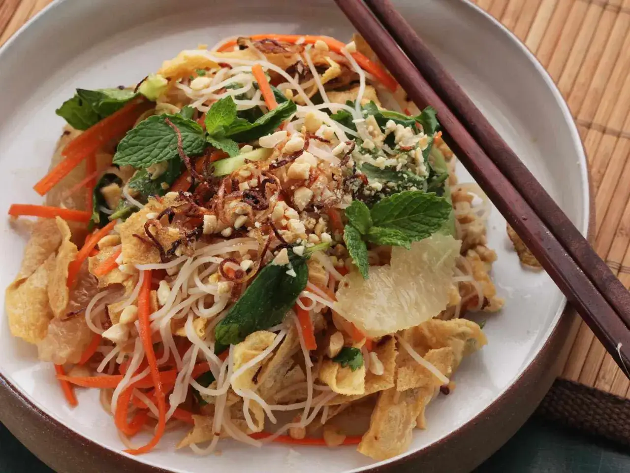 Asia Nudel-Salat mit Karotten, Erdnüssen und Minze, garniert mit knusprigen Zwiebeln.