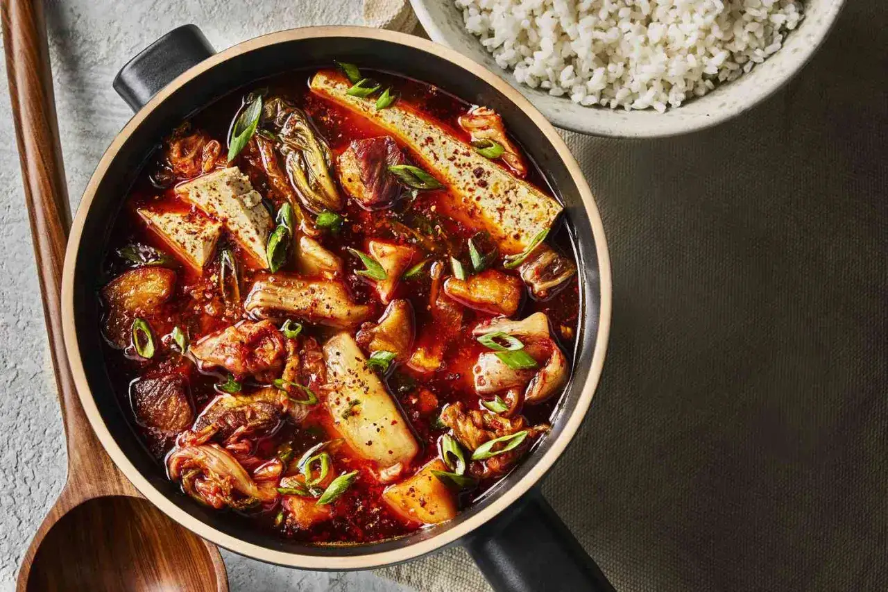 Herzhafte Kimchi Suppe mit Tofu, Fleisch und Frühlingszwiebeln, daneben eine Schüssel Reis.