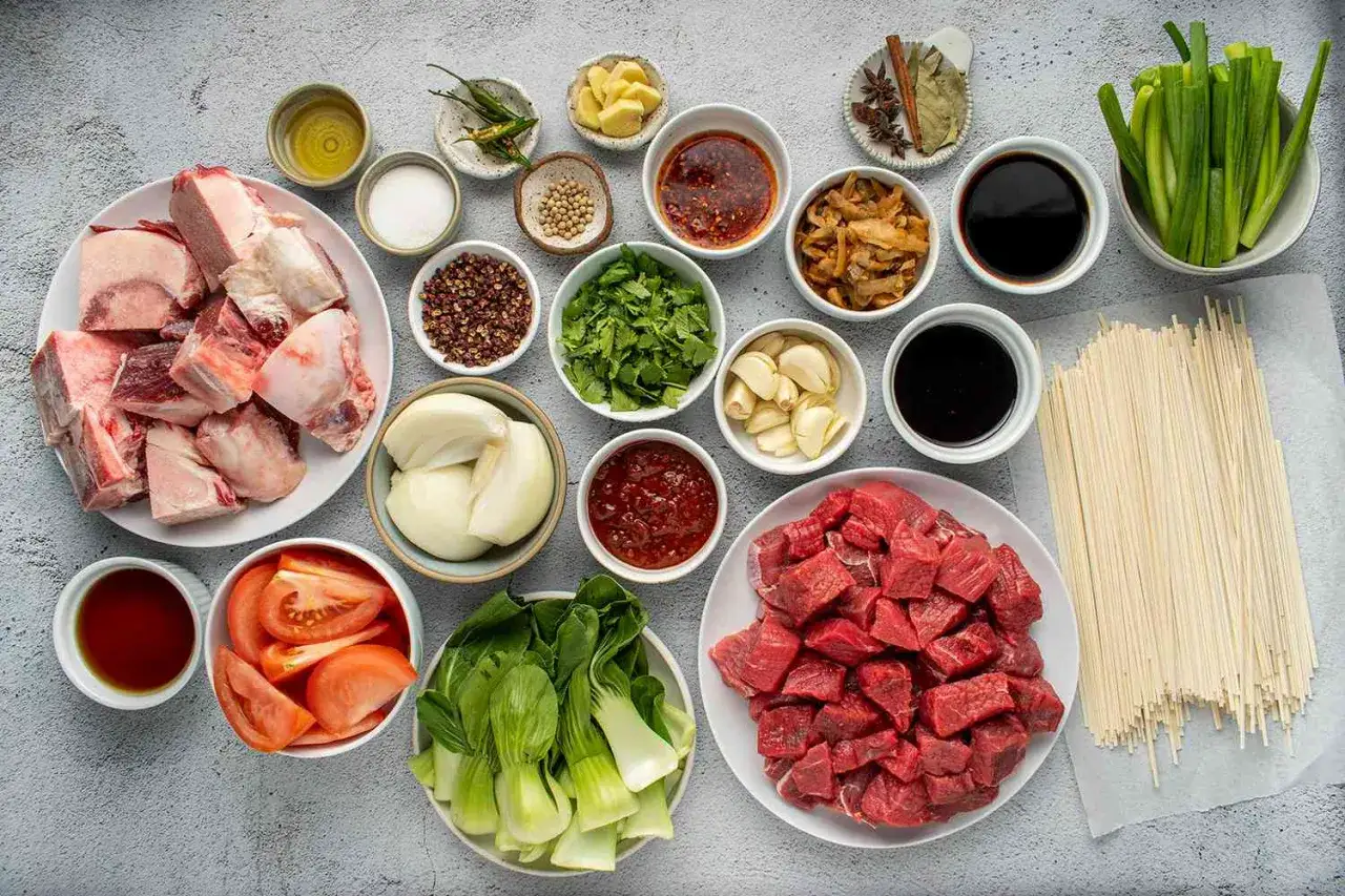 Zutaten für Niu Rou Mian: Rindfleischwürfel, Knochen, Tomaten, Pak Choi, Nudeln, Zwiebeln, Knoblauch, Ingwer, Chili, Sojasauce, Gewürze.