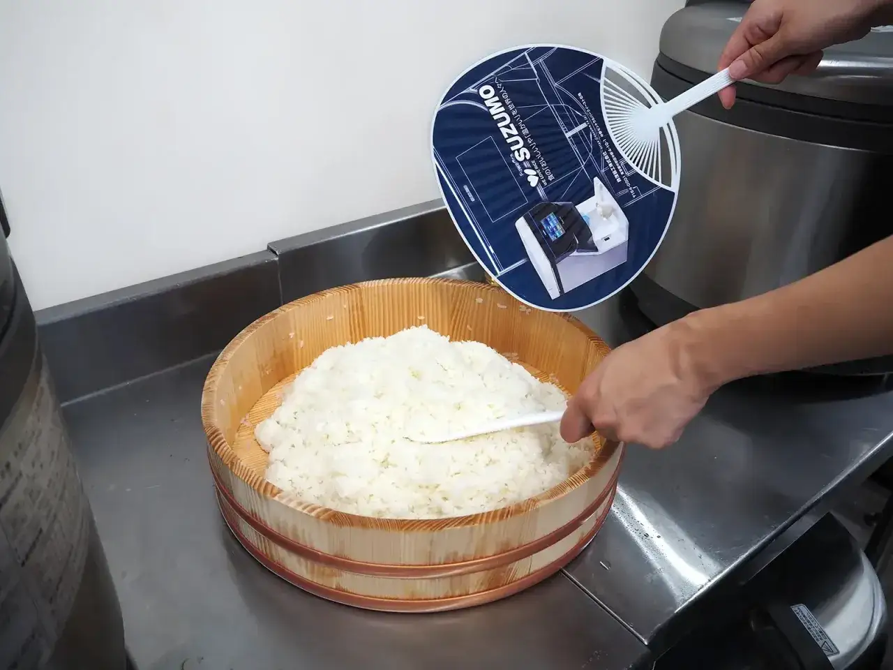 Frischer Reis wird in einer hölzernen Schüssel für das Sushi Essig Rezept gekühlt. Ein Fächer mit technischen Zeichnungen wird benutzt.
