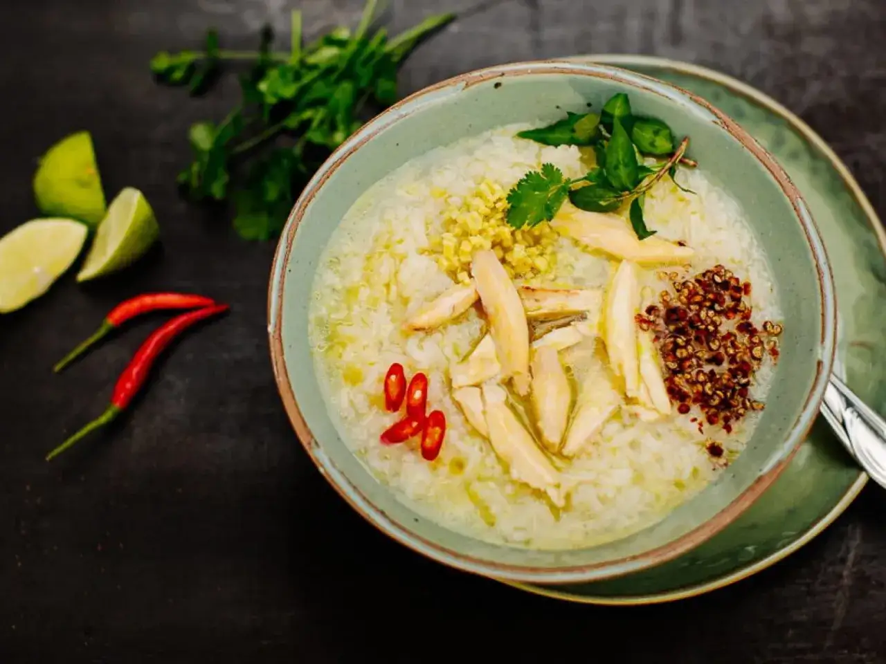 Eine Sch&uuml;ssel mit vietnamesischer Reissuppe, garniert mit H&uuml;hnchen, Kr&auml;utern, Chili und Limettenspalten.