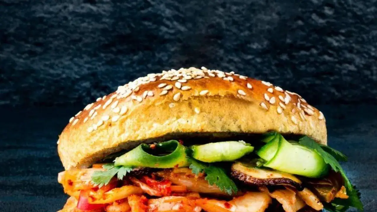 Ein köstlicher koreanischer Burger mit Kimchi, Gurkenscheiben und Koriander auf einem Sesambrötchen.