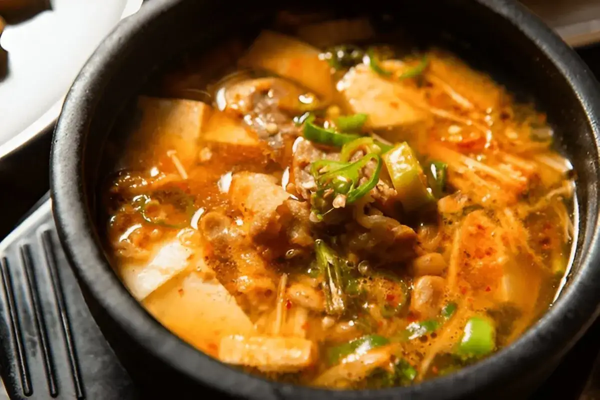Herzhafter Eintopf mit Tofu, Fleisch und Pilzen in würziger Doenjang-Sauce, garniert mit grünen Chilis.