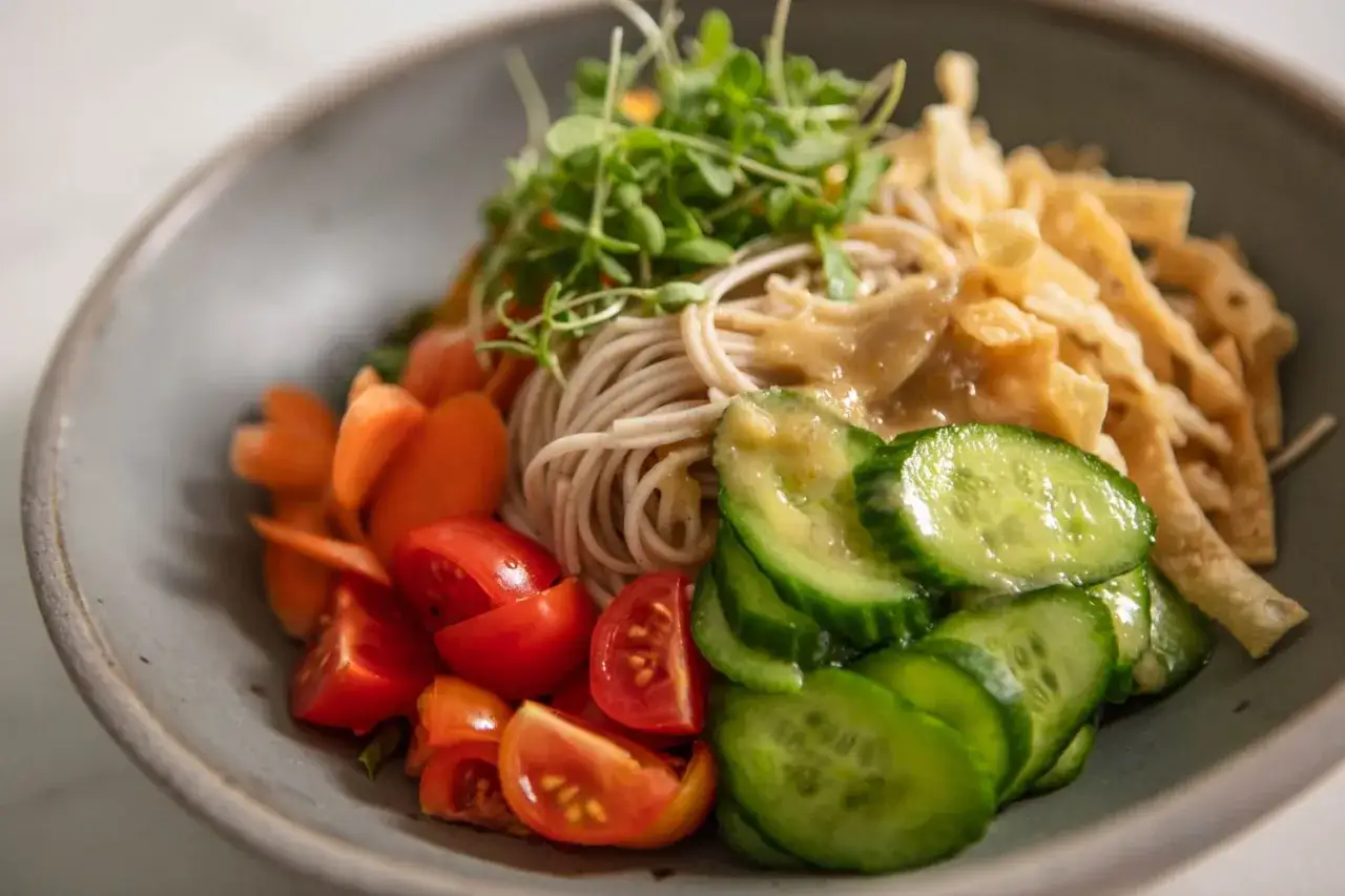 Erfrischender soba nudelsalat mit knackigen Karotten, Kirschtomaten, Gurkenscheiben und Sprossen, serviert in einer grauen Schüssel.