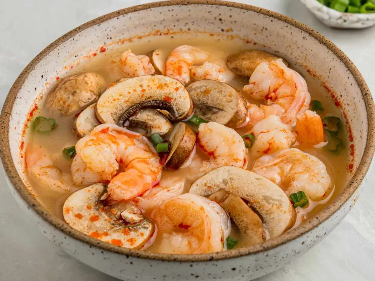 Eine Schüssel mit aromatischem Tom Yam Gung, gefüllt mit saftigen Garnelen und Pilzen, garniert mit Frühlingszwiebeln und Chili.