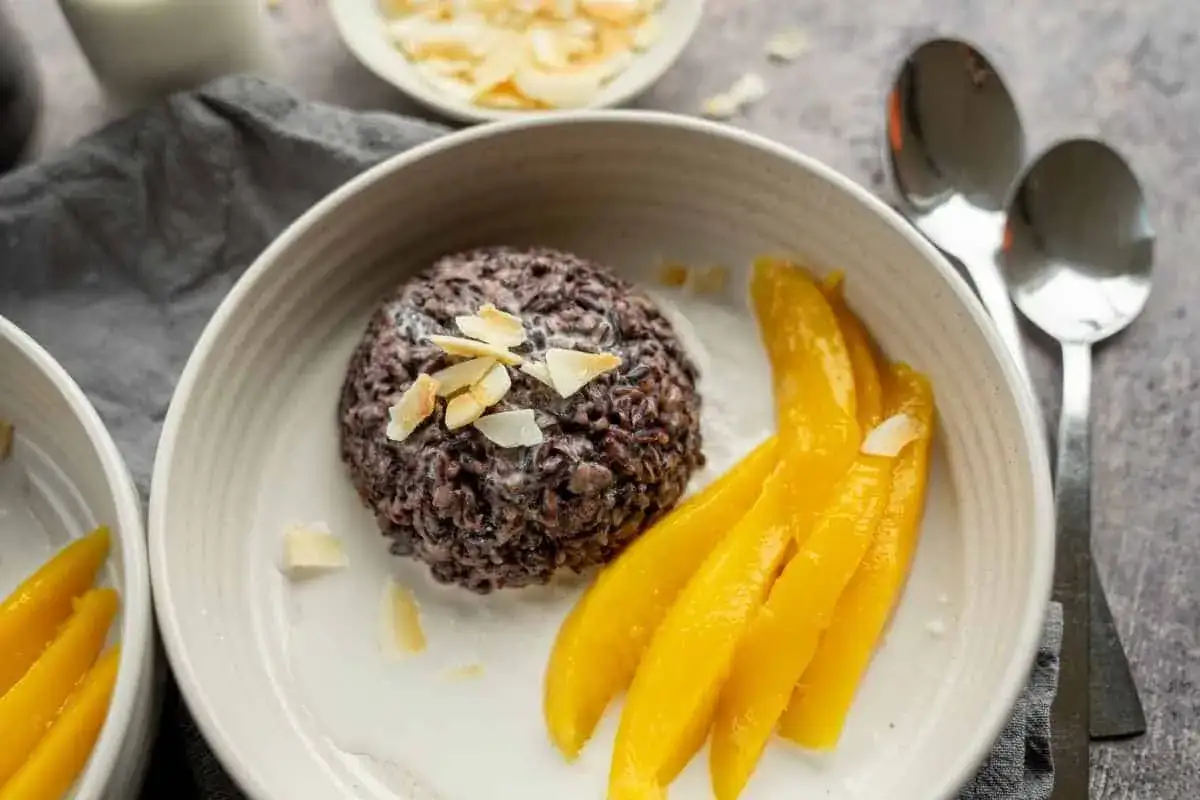 Schwarzer Klebreis mit Kokosmilch, garniert mit Mandelbl&auml;ttchen, serviert mit saftigen Mangostreifen. Ein s&uuml;&szlig;er Genuss.