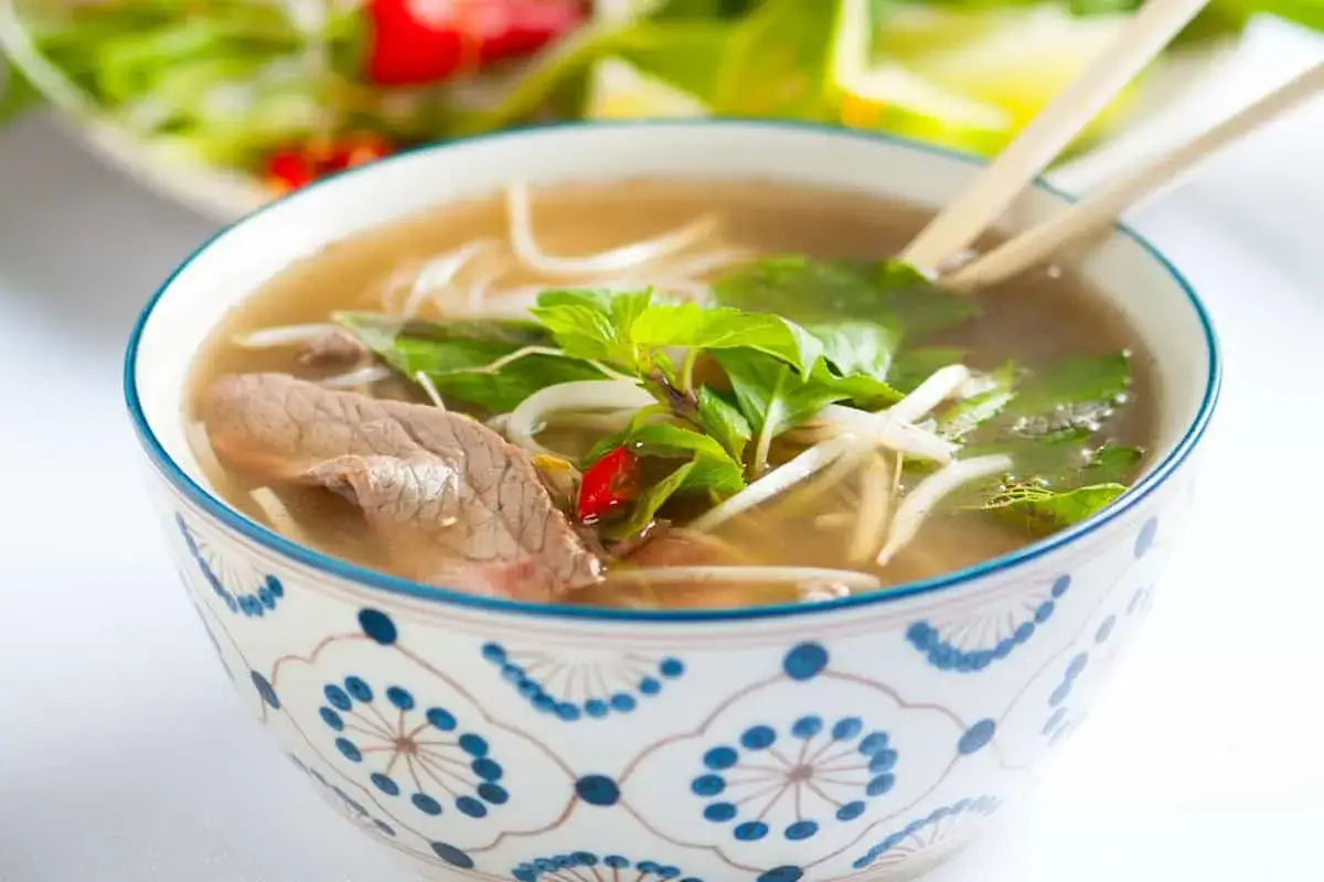 Herzhaftes Pho-Rezept: Eine Sch&uuml;ssel dampfender Rindfleisch-Pho mit Reisnudeln, frischen Kr&auml;utern und Chili.