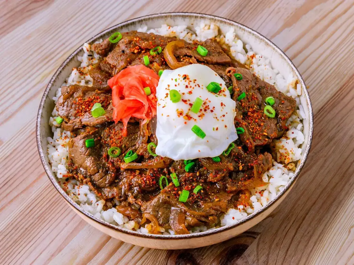 Eine japanische Bowl mit Reis, zartem Rindfleisch, einem pochierten Ei, eingelegtem Ingwer und Fr&uuml;hlingszwiebeln.