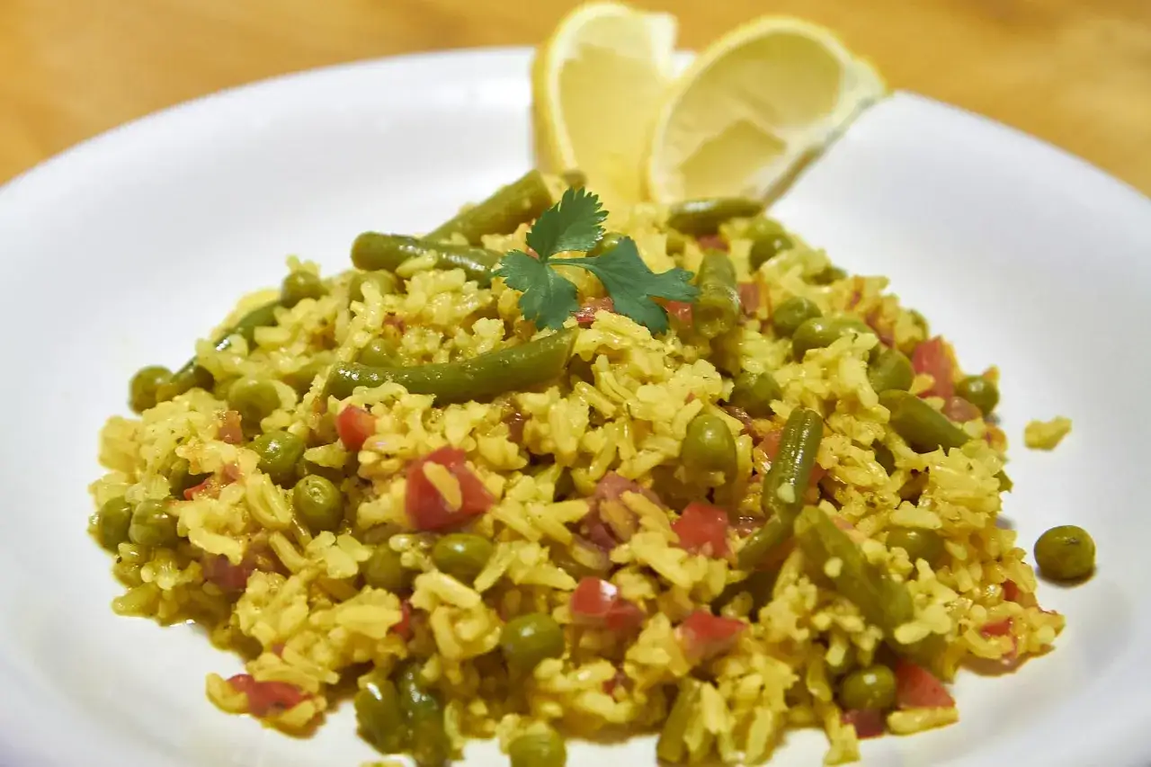 Ein Teller mit aromatischem Pilaw Reis, garniert mit gr&uuml;nen Bohnen, Erbsen, Tomatenw&uuml;rfeln und Zitronenspalten.