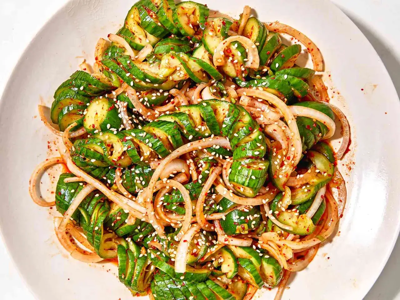 Ein erfrischender asiatischer Gurkensalat mit Zwiebeln, Sesam und Gew&uuml;rzen, serviert auf einer Platte.