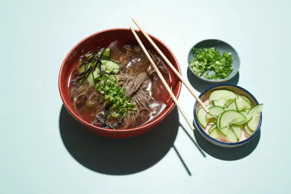 Erfrischendes Mul Naengmyeon mit Buchweizennudeln, Gurkenscheiben, Frühlingszwiebeln und Seetang.